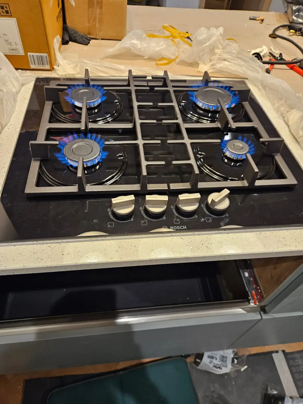 Four-burner glass gas hob with all burners lit after installation and safety testing