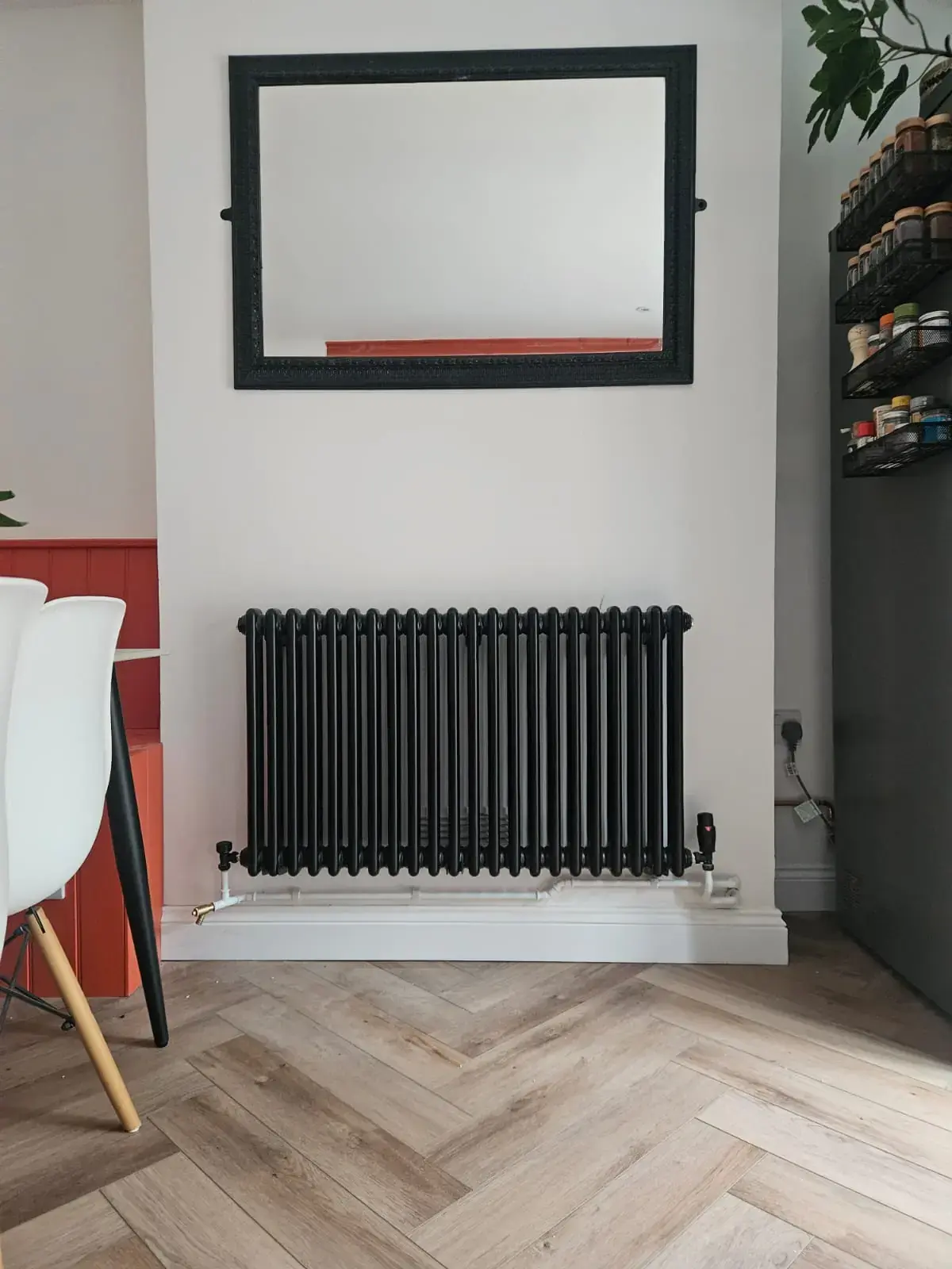 Black horizontal column radiator fitted in a dining room above a herringbone wood floor