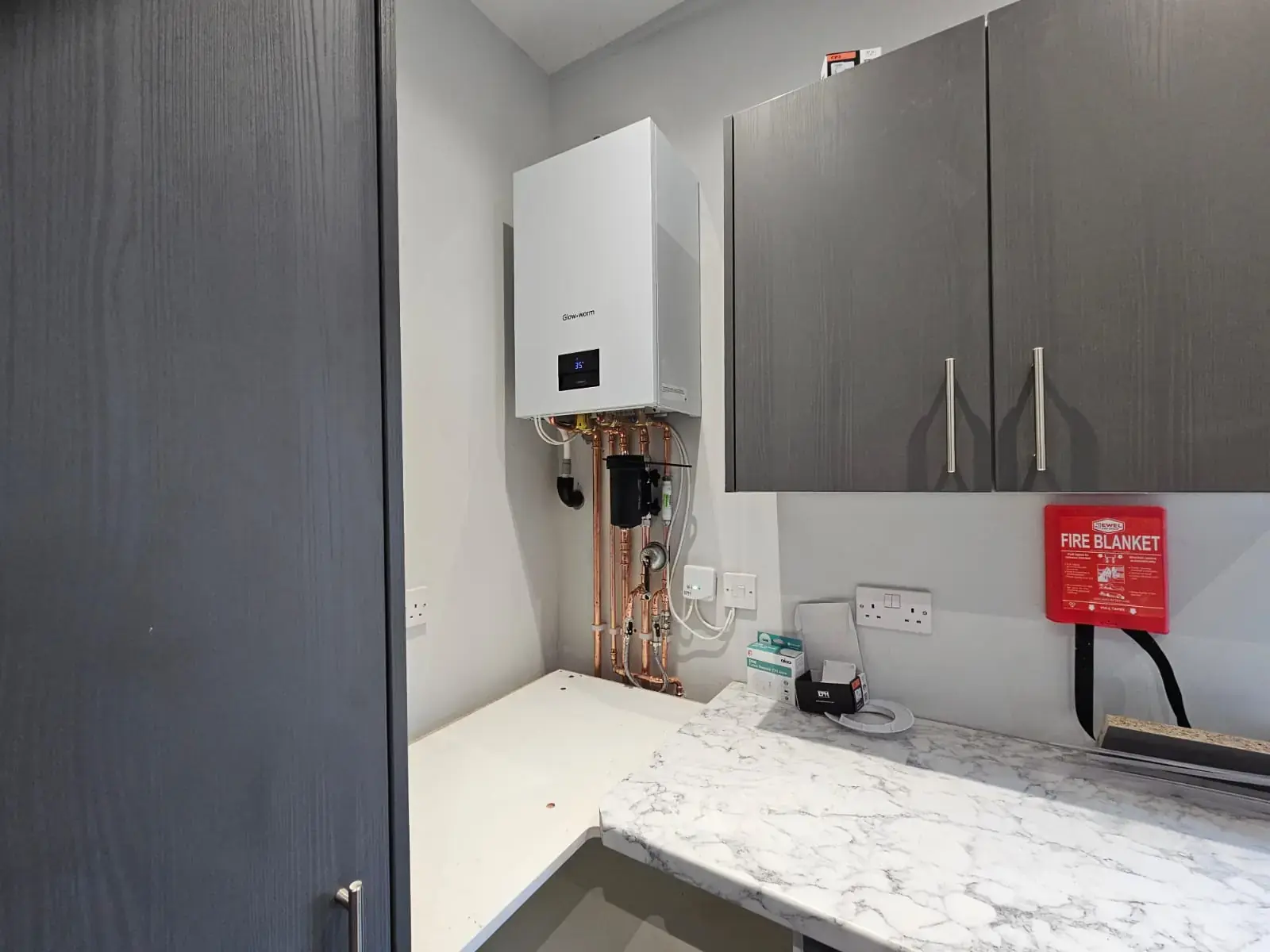 Combi boiler installed beside grey kitchen wall units above a marble-effect worktop