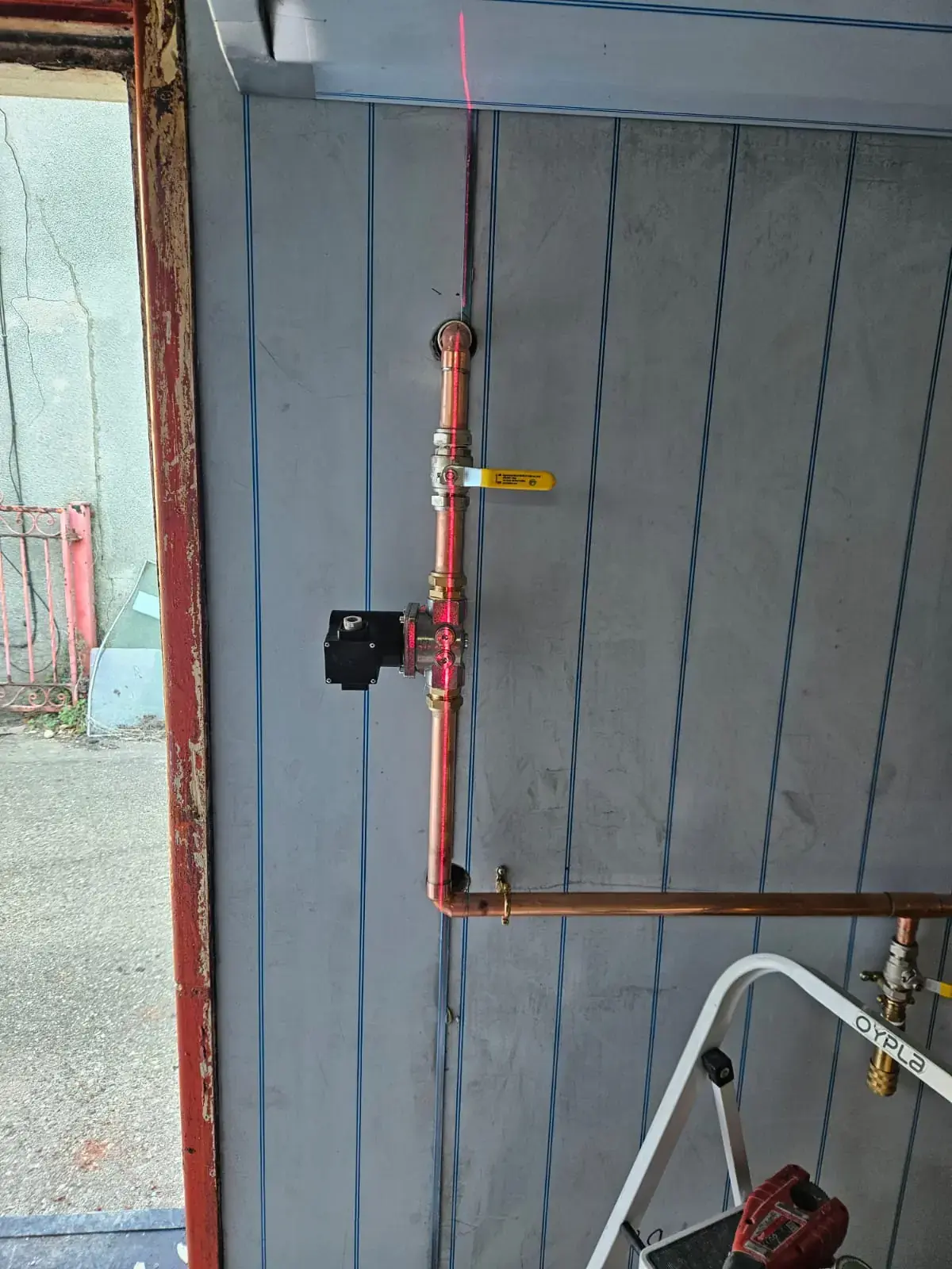 Gas supply pipe with solenoid valve and yellow isolation handle on a commercial kitchen wall